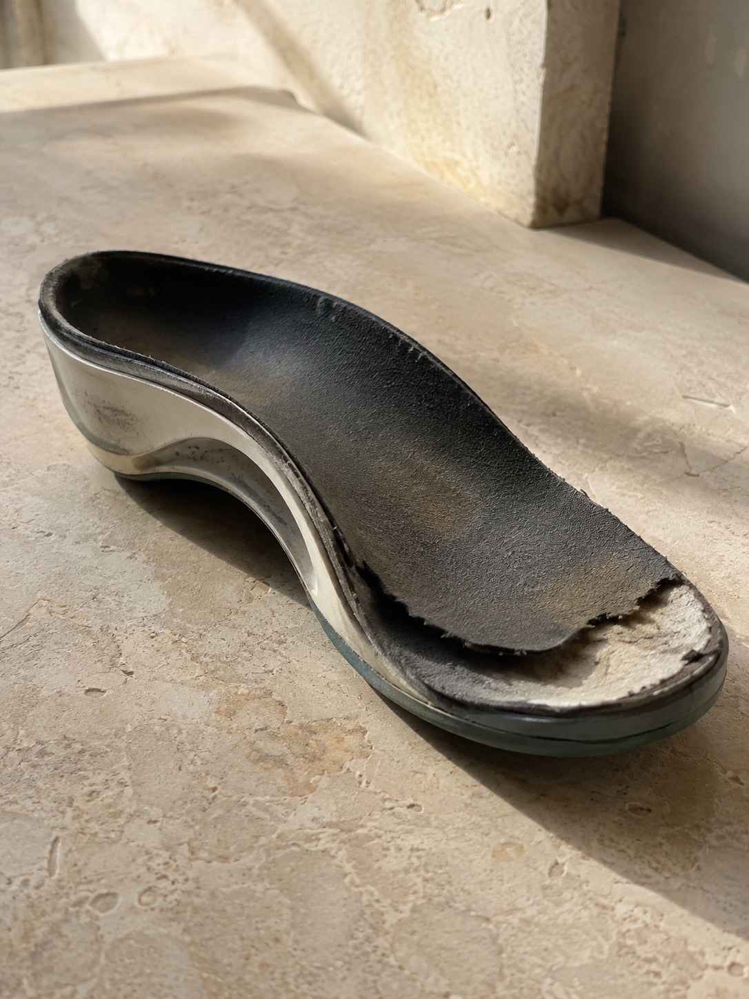 A worn custom orthotic with a degraded top cover over an intact shell